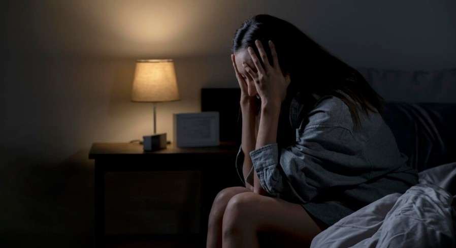Mulher sentada na cama com as mãos na cabeça com sintomas de ansiedade